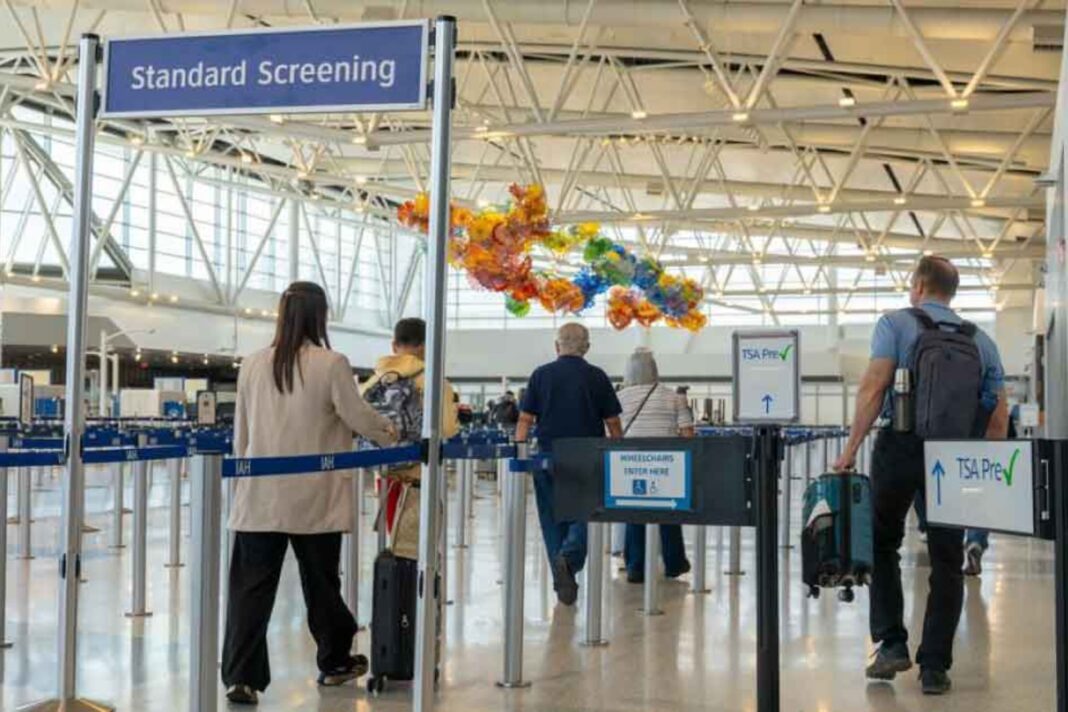Fila de pasajeros en un aeropuerto internacional con carteles en inglés y español.